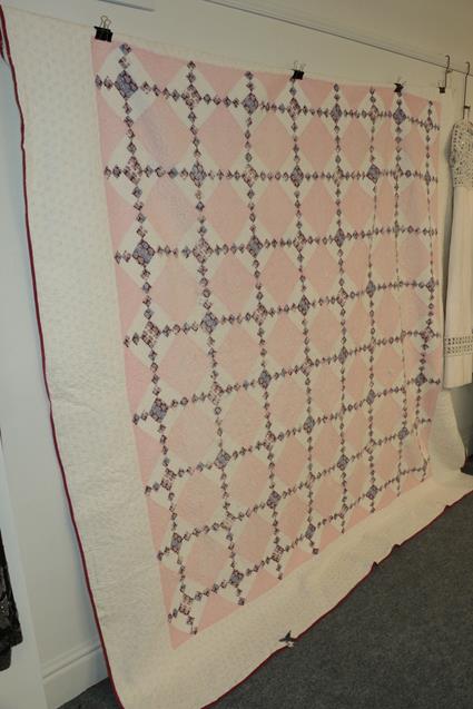 Large white cotton quilt appliqued with pink diamond shaped patchworks and interspersed with smaller