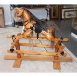 A carved wooden rocking horse with tack on a trestle base, 153cm by 115cm high