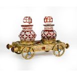 A Gilt-Metal, Gem-Set and Enameled Bottle-Stand, in the form of a flatbed rail carriage, set with