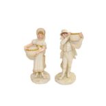 A pair of Royal Worcester figures of a boy and a girl holding a basket, reclined against a tree