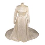 A 1962 Jean Varon Wedding Dress, in cream silk with long sleeves and shaped cuffs, scooped neck, bow