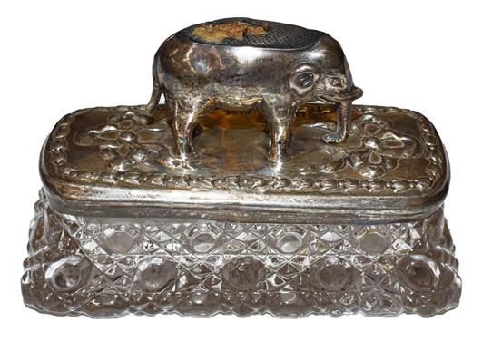 An Edwardian silver elephant pin cushion, mounted on the lid of a cut glass pin box, repaired,