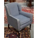 An Edwardian wingback upholstered armchair, raised on square mahogany supports with castors