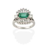 An Emerald and Diamond Cluster Ring, the central step cut emerald flanked by two round brilliant cut