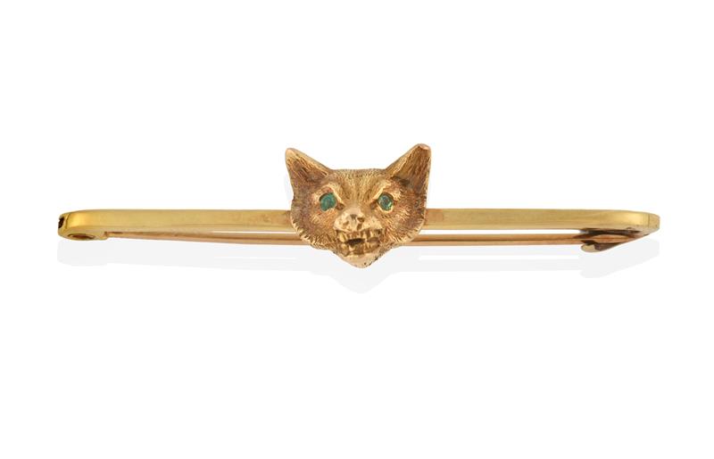 A Fox Mask Bar Brooch, the textured yellow fox mask with round cut emerald eyes, to a knife edge