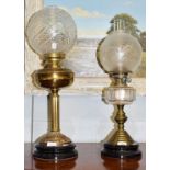 Two Victorian brass oil lamps with glass shades, one with a clear glass reservoir, the other with