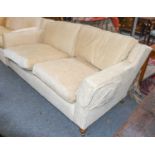 A modern upholstered three-seater sofa, champagne upholstery on turned supports with brass