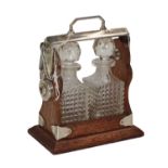 An oak miniature two bottle tantalus with silver plated mounts and pair of moulded glass bottles,
