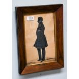 An early 19th century silhouette of a gentleman, standing wearing a frock coat, with white