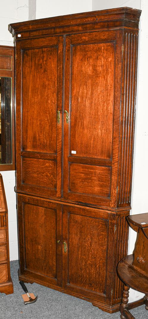 A large Georgian oak standing corner cupboard, with panelled doors and fluted pillasters, 114cm by