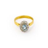 An 18 carat gold aquamarine and diamond cluster ring, the oval cut aquamarine within a border of