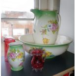 Two cranberry glass vases and a floral patterned jug and basin