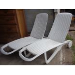 Pair of white plastic garden sun loungers on wheels with cushions