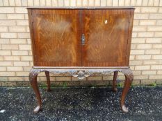 A twin door drinks cabinet with carved decoration, raised on cabriole supports,