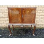 A twin door drinks cabinet with carved decoration, raised on cabriole supports,