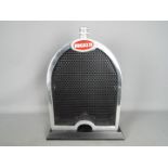 A chrome Bugatti style radiator set on a plinth,
