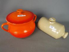 A volcanic orange Le Creuset lidded soup tureen and a vintage stoneware bed warmer.