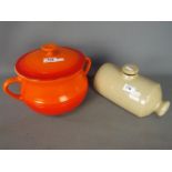 A volcanic orange Le Creuset lidded soup tureen and a vintage stoneware bed warmer.
