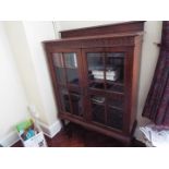 A freestanding glazed bookcase having twin doors with carved decoration,