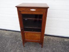 An Edwardian mahogany cabinet, the glazed door opening to reveal a four-tier shelved interior,