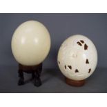 Two blown ostrich eggs (Struthio camelus), one with carved decoration, on stands.