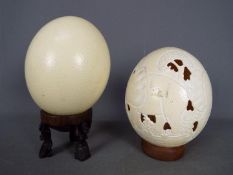 Two blown ostrich eggs (Struthio camelus), one with carved decoration, on stands.