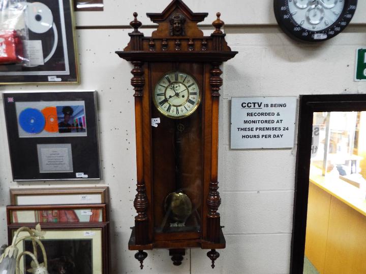 A highly carved walnut double weight Vienna wall clock with ceramic dial and pendulum