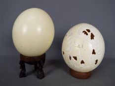 Withdrawn - Two blown ostrich eggs (Struthio camelus), one with carved decoration, on stands.