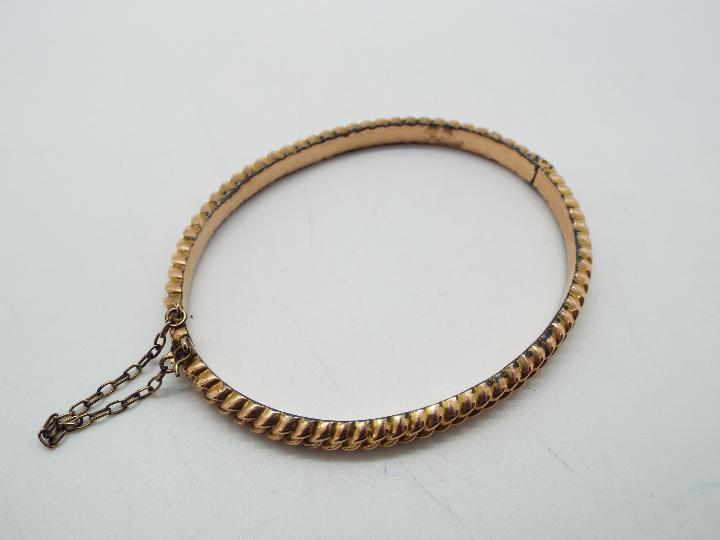 A 9ct gold hinged bangle with safety chain, approximately 6 grams all in.