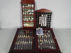 A collection of collector spoons and souvenir thimbles contained within four display cases.