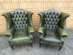 A pair of green leather wingback chairs.