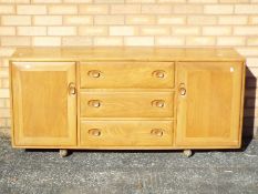 An Ercol sideboard having a central section of three drawers flanked by cupboards,