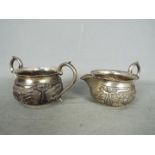 Indian Silver - A cream jug and twin handled sugar bowl each with repoussé decoration and stamped