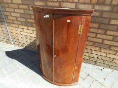 A Georgian wall mounted, cylinder front corner cabinet having three fixed shelves within,