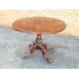 A Victorian flip top round table supported on a central stem on a carved quadripartite base,