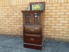 A mahogany commode with carved detail, brass drop handles, mirror top,