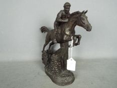 A cold cast bronze figurine depicting a racehorse and jockey clearing a fence,