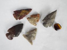 Five knapped arrow heads and a piece of tiger's eye quartz.