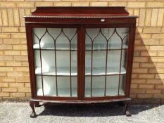 A twin door glazed bookcase or display cabinet, having bow front and carved detailing,
