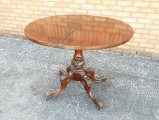 A Victorian flip top round table supported on a central stem on a carved quadripartite base,
