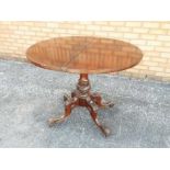 A Victorian flip top round table supported on a central stem on a carved quadripartite base,