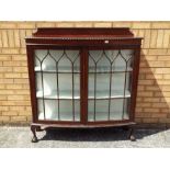 A twin door glazed bookcase or display cabinet, having bow front and carved detailing,