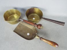 A vintage brass sauce pan with wooden handle and a brass sauce pan with brass shovel