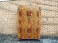 A burr walnut veneered twin door wardrobe with carved detailing,