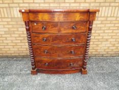 A flame mahogany veneered chest of drawers, bow front and flanked by barley twist columns,