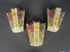 Three Arthur Wood, Art Deco, wall pockets with floral decoration and silvered rims,