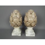 A pair of ceramic artichokes raised on unglazed, marble effect plinths, approximately 28 cm (h).
