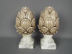 A pair of ceramic artichokes raised on unglazed, marble effect plinths, approximately 28 cm (h).