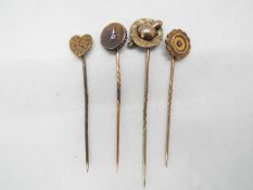 Four yellow metal stick pins, two of which are stone set, each contained in a case.