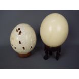 LOT WITHDRAWN - Two blown ostrich eggs (Struthio camelus), one with carved decoration, on stands.